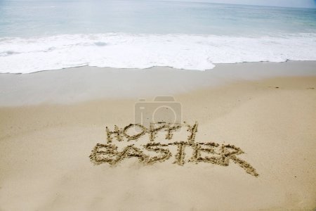 Foto de Semana Santa Hoppy. Las palabras HOPPY EASTER escritas en la arena junto al océano. - Imagen libre de derechos