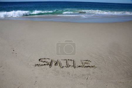 Foto de Smile written in the sand on the beach.  message handwritten on a smooth sand beach - Imagen libre de derechos