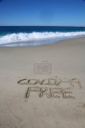 Téléchargez les photos : Covid-19 free written in the sand on the beach.  message handwritten on a smooth sand beach - en image libre de droit