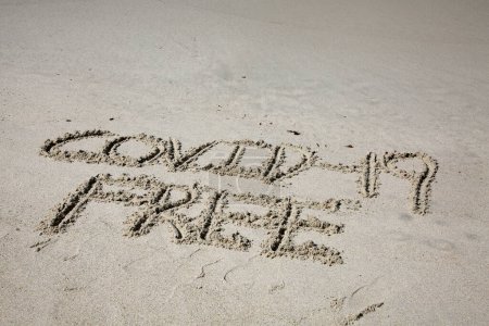 Téléchargez les photos : Covid-19 free written in the sand on the beach.  message handwritten on a smooth sand beach - en image libre de droit
