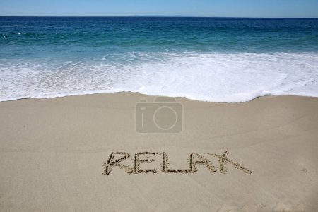 Foto de Relax written in the sand on the beach.  message handwritten on a smooth sand beach - Imagen libre de derechos