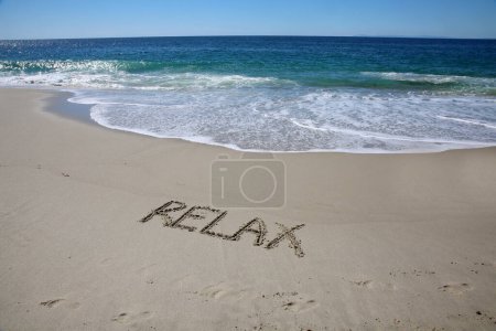 Foto de Relax  written in the sand on the beach.  message handwritten on a smooth sand beach - Imagen libre de derechos
