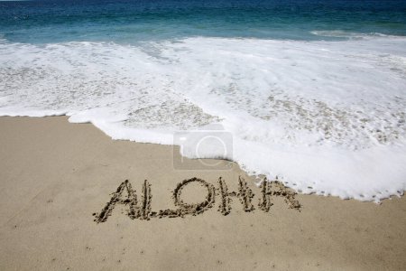 Foto de Aloha written in the sand on the beach.  message handwritten on a smooth sand beach - Imagen libre de derechos