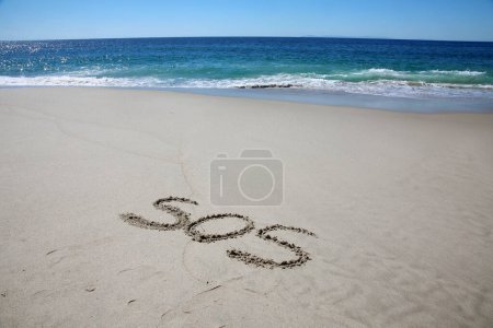 Téléchargez les photos : Sos written in the sand on the beach.  message handwritten on a smooth sand beach - en image libre de droit