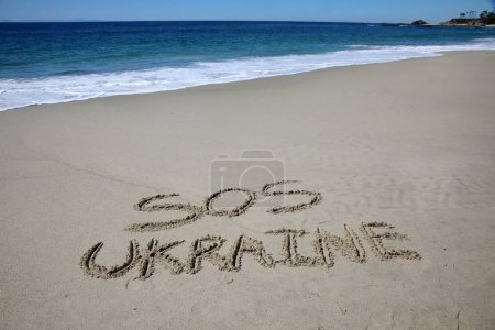 Foto de Sos  ukraine written in the sand on the beach.  message handwritten on a smooth sand beach - Imagen libre de derechos