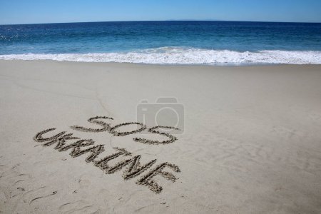 Foto de Sos ukraine written in the sand on the beach.  message handwritten on a smooth sand beach - Imagen libre de derechos