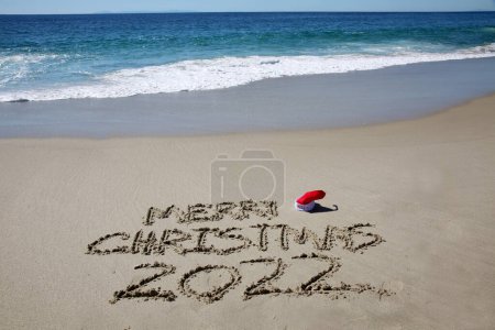 Téléchargez les photos : Merry christmas written in the sand on the beach.  message handwritten on a smooth sand beach - en image libre de droit