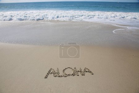 Téléchargez les photos : Aloha  written in the sand on the beach.  message handwritten on a smooth sand beach - en image libre de droit
