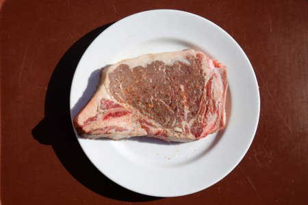 Foto de Steak. Beef Stake. Fresh raw beef steak. Raw Meat. Steak on a White Plate. Raw Meat on a ceramic plate. T-Bone steak. Cut of Beef. Grilled Meat. Porterhouse. Rib-eye. Top Sirloin. - Imagen libre de derechos
