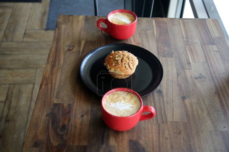 Téléchargez les photos : Latte avec un muffin aux noix de banane. Café avec un muffin sur une assiette noire dans un café. Petit déjeuner Muffin et café avec Latte Art dans la mousse pour le petit déjeuner ou une collation dans un café. Petit déjeuner. - en image libre de droit
