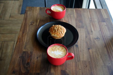 Foto de Latte con un Muffin de nuez de plátano. Café con una magdalena en un plato negro en una cafetería. Desayuno Muffin y Café con Latte Art en la espuma para el desayuno o un aperitivo en una cafetería. Desayuno. - Imagen libre de derechos