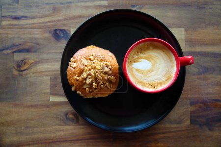 Téléchargez les photos : Latte with a Banana Walnut Muffin. Coffee with a Muffin on a black plate in a Coffee Shop. Breakfast Muffin and Coffee with Latte Art in the foam for breakfast or a snack in a Coffee Shop. Breakfast. - en image libre de droit