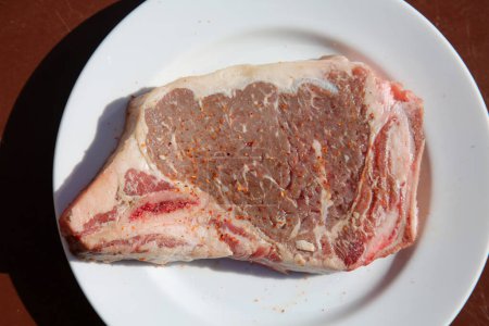 Photo for Steak. Beef Stake. Fresh raw beef steak. Raw Meat. Steak on a White Plate. Raw Meat on a ceramic plate. T-Bone steak. Cut of Beef. Grilled Meat. Porterhouse. Rib-eye. Top Sirloin. - Royalty Free Image