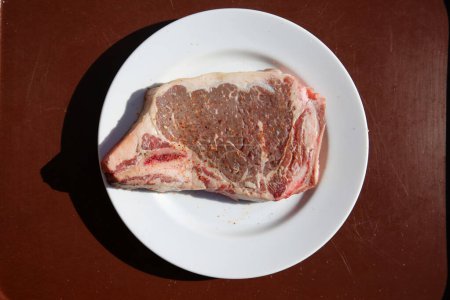 Foto de Steak. Beef Stake. Fresh raw beef steak. Raw Meat. Steak on a White Plate. Raw Meat on a ceramic plate. T-Bone steak. Cut of Beef. Grilled Meat. Porterhouse. Rib-eye. Top Sirloin. - Imagen libre de derechos