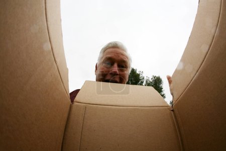 Photo for Opening a Carboard Box. Smiling man opening a carton box, relocation and unpacking concept. Concept of delivery, surprise, gift, person opening a cardboard box. A surprised man unpacking a box. - Royalty Free Image