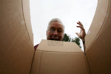 Téléchargez les photos : Ouverture d'une boîte en carton. Homme souriant ouvrant une boîte en carton, concept de déménagement et de déballage. Concept de livraison, surprise, cadeau, personne ouvrant une boîte en carton. Un homme surpris déballer une boîte. - en image libre de droit