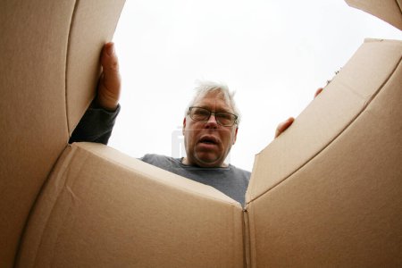 Photo for Opening a Carboard Box. Smiling man opening a carton box, relocation and unpacking concept. Concept of delivery, surprise, gift, person opening a cardboard box. A surprised man unpacking a box. - Royalty Free Image