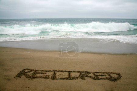 Téléchargez les photos : Retraité écrit dans le sable de plage avec l'océan comme arrière-plan. - en image libre de droit