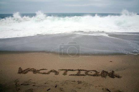 Foto de Vacaciones escritas en arena de playa con el océano como fondo. - Imagen libre de derechos