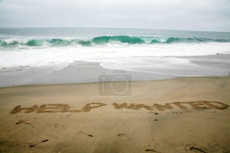 Téléchargez les photos : Aide voulait écrit dans le sable de plage avec l'océan comme arrière-plan. - en image libre de droit