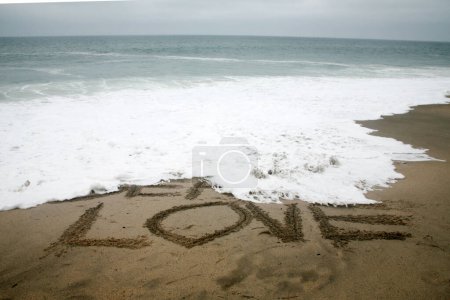 Téléchargez les photos : Mer d'amour écrit dans le sable de plage avec l'océan comme arrière-plan. - en image libre de droit