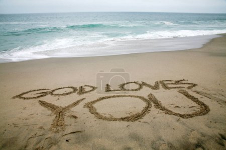 Foto de Dios te ama escrito en arena de playa con el océano como fondo. - Imagen libre de derechos