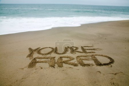Foto de Estás despedido escrito en la arena de la playa con el océano como fondo. - Imagen libre de derechos