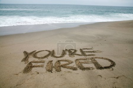 Foto de Estás despedido escrito en la arena de la playa con el océano como fondo. - Imagen libre de derechos