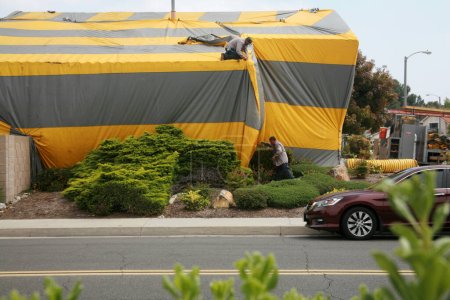 Téléchargez les photos : Irvine, Californie - États-Unis - 17 mai 2023 : Maison de style ranch recouverte d'une tente termite jaune et gris. Une maison d'habitation couverte d'une tente en toile jaune et grise tout en étant fumigée pour les termites. - en image libre de droit