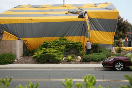 Foto de Irvine, California - Estados Unidos - 17 de mayo de 2023: Casa de estilo rancho cubierta de tienda de termitas amarillas y grises. Una casa residencial cubierta con una carpa de lona amarilla y gris mientras se fumigaba para termitas. - Imagen libre de derechos