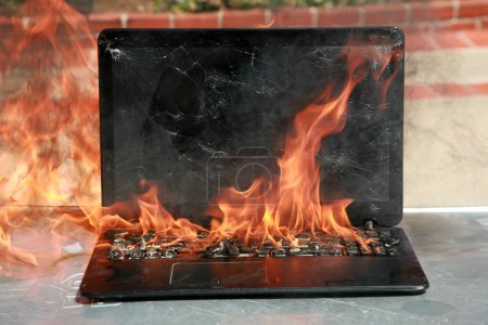 Téléchargez les photos : Brûlage d'un ordinateur portable et d'un clavier, incendie d'équipement dû à une batterie et à un câblage défectueux. L'ordinateur portable brûle en flammes. Risque d'incendie. - en image libre de droit