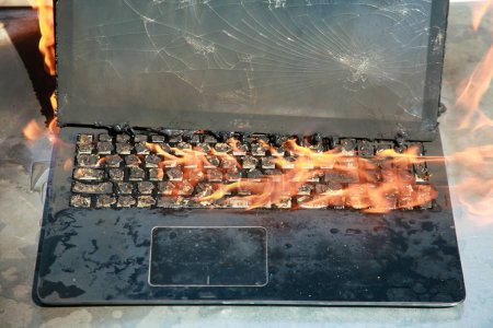 Photo for Burning laptop and keyboard, equipment fire due to faulty battery and wiring. Laptop burning in flames. Fire hazard. - Royalty Free Image