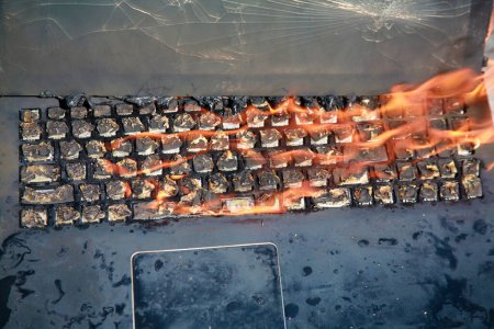 Foto de Quemar el ordenador portátil y el teclado, fuego del equipo debido a la batería defectuosa y el cableado. Computadora portátil en llamas. Peligro de incendio. - Imagen libre de derechos