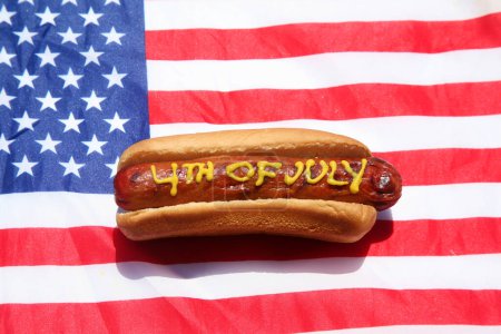 Foto de Perro caliente. Mostaza en salchicha patriótica. 4 de julio Hot Dog. 4 de julio escrito en Yellow Mustard on a Hotdog. Estados Unidos Patriotic picnic holiday hotdogs. - Imagen libre de derechos