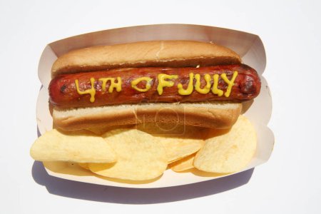 Téléchargez les photos : Hotdog avec le texte du 4 juillet écrit en moutarde jaune. Hotdogs pour le déjeuner. Isolé sur blanc. - en image libre de droit