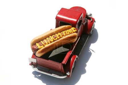 Téléchargez les photos : Hotdog avec les mots heure du déjeuner écrit en moutarde jaune. Hotdogs pour le déjeuner. Isolé sur blanc. Hotdog dans un camion rouge dans son chignon. - en image libre de droit