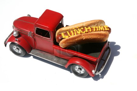 Foto de Hotdog con las palabras hora del almuerzo escritas en mostaza amarilla. Perros calientes para el almuerzo. Aislado sobre blanco. Hotdog en un camión rojo en su moño. - Imagen libre de derechos