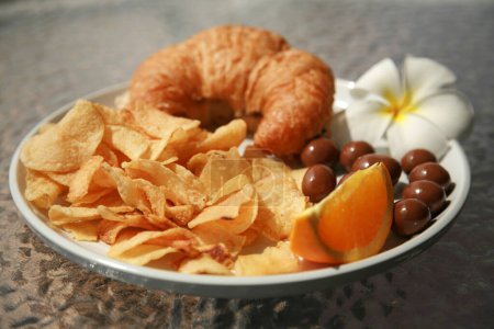 Photo for Lunch. Hawaiian Lunch. Turkey Croissant Sandwich with Chips an Orange Section and Chocolate Covered Macadamia Nuts. - Royalty Free Image