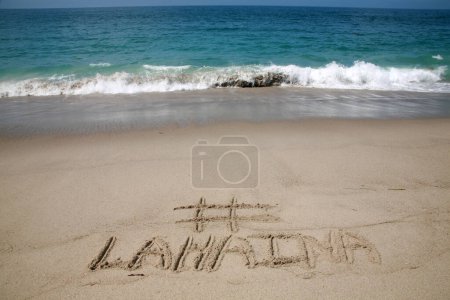 Téléchargez les photos : Le nom # LAHAINA écrit dans le sable sur la plage avec le fond de l'océan Pacifique - en image libre de droit