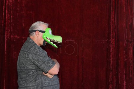 Photo for Man in crocodile mask posing for his picture to be taken while in a photo booth at a party - Royalty Free Image