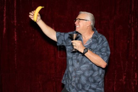 Photo for A man takes selfie on banana while having his picture taken in a Photo Booth at a party. People love photo booths at parties and events. - Royalty Free Image