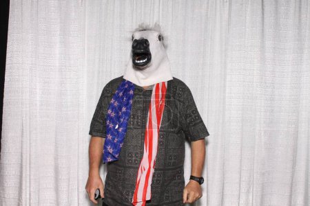 Téléchargez les photos : Personne non identifiable porte un masque de tête de cheval et une écharpe avec un drapeau américain, pose pendant que ses photos sont prises dans une cabine photo. - en image libre de droit