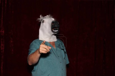 Téléchargez les photos : Un homme portant un masque de tête de cheval en caoutchouc pose pendant qu'il se fait prendre en photo dans une cabine photo. - en image libre de droit