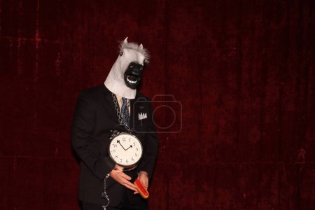 Foto de Un hombre con una máscara de cabeza de caballo de goma posa y sostiene apoyos mientras tiene sus fotos tomadas mientras está en una cabina de fotos. - Imagen libre de derechos