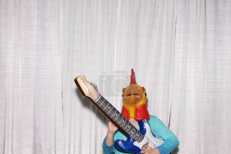 Photo for A man wears Cock head mask and poses with guitar while waiting for his pictures to be taken in a Photo Booth. - Royalty Free Image