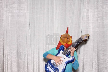 Photo for A man wears Cock head mask and poses with guitar while waiting for his pictures to be taken in a Photo Booth. - Royalty Free Image