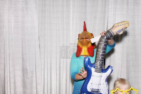 Téléchargez les photos : Un homme porte un masque de tête de bite et pose à la guitare en attendant que ses photos soient prises dans une cabine photo. - en image libre de droit