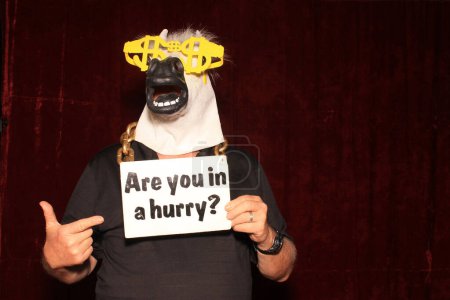 Foto de Un hombre con una máscara de cabeza de caballo de goma posa y sostiene apoyos mientras tiene sus fotos tomadas mientras está en una cabina de fotos. - Imagen libre de derechos