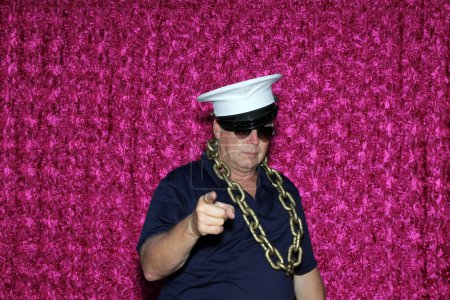 Photo for Man wears white cap and sunglasses and poses for his picture to be taken while in a Photo Booth at a Party. - Royalty Free Image