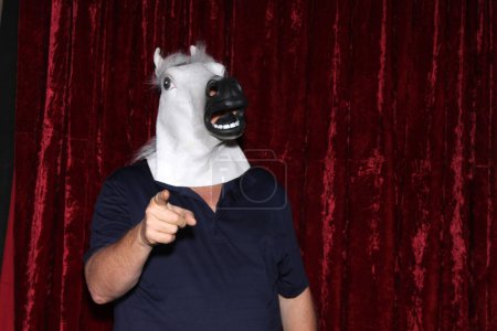 Téléchargez les photos : Un homme portant un masque de tête de cheval en caoutchouc pose pendant qu'il se fait prendre en photo dans une cabine photo. - en image libre de droit